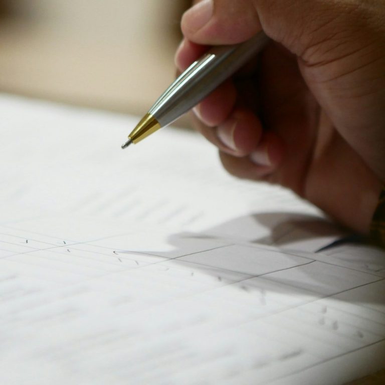 Eine Hand hält einen Stift über einem Blatt mit Text und Linien.