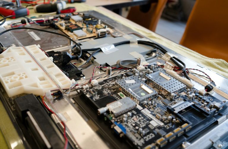 Offenes Elektronikgerät mit sichtbaren Platinen und Kabeln auf einem Tisch.